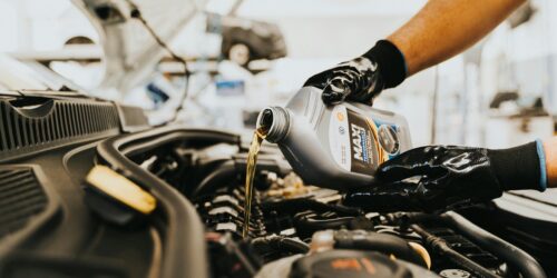 Een fles versnellingsbakolie, 2-takt olie en een olieopvangbak op een werkbank, klaar voor gebruik bij motoronderhoud.