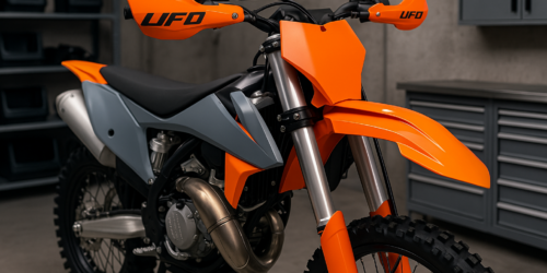 Motocross motor met nieuwe oranje/grijze UFO plastic kit en UFO handkappen, gemonteerd met bijpassende bevestiging set in een professionele werkplaats.
