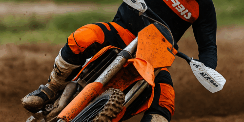 Een motorcrosser in volledige Acerbis outfit rijdt door een modderige bocht, met handkappen en bodyprotector zichtbaar tijdens actie op het circuit