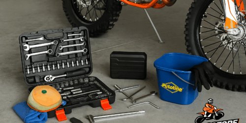 Een goed gevulde gereedschapskoffer ligt open naast een KTM crossmotor, met t-sleutels, jumpstarter en luchtfiltermateriaal klaar voor gebruik